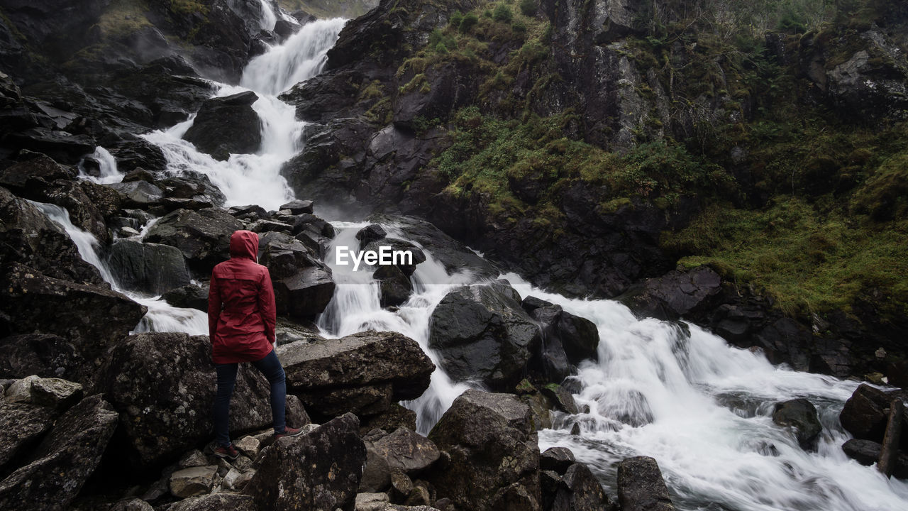 Rear view of woman standing by waterfall on rock