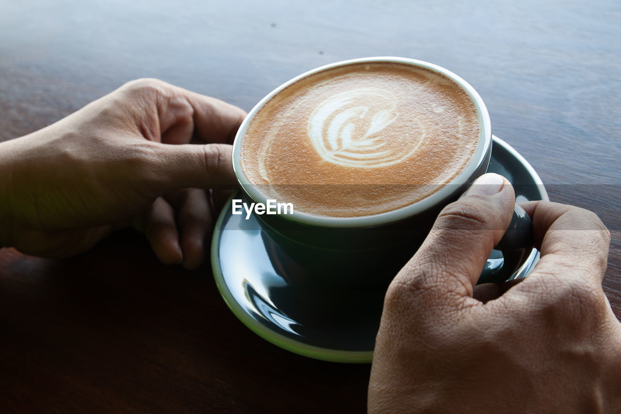 CLOSE-UP OF HAND HOLDING COFFEE CUP AND SPOON ON TABLE