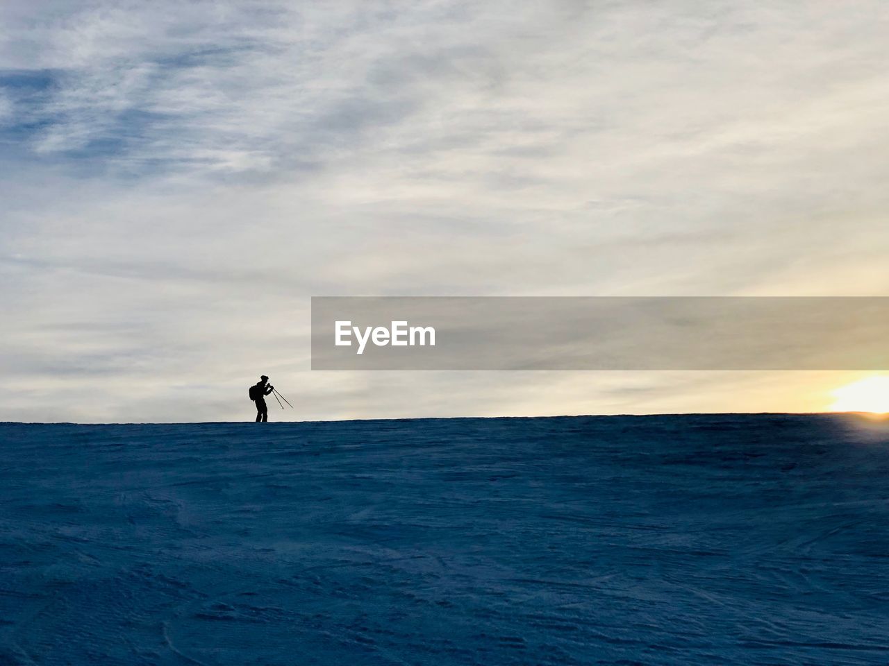 Silhouette woman standing on snow covered field against cloudy sky during sunset