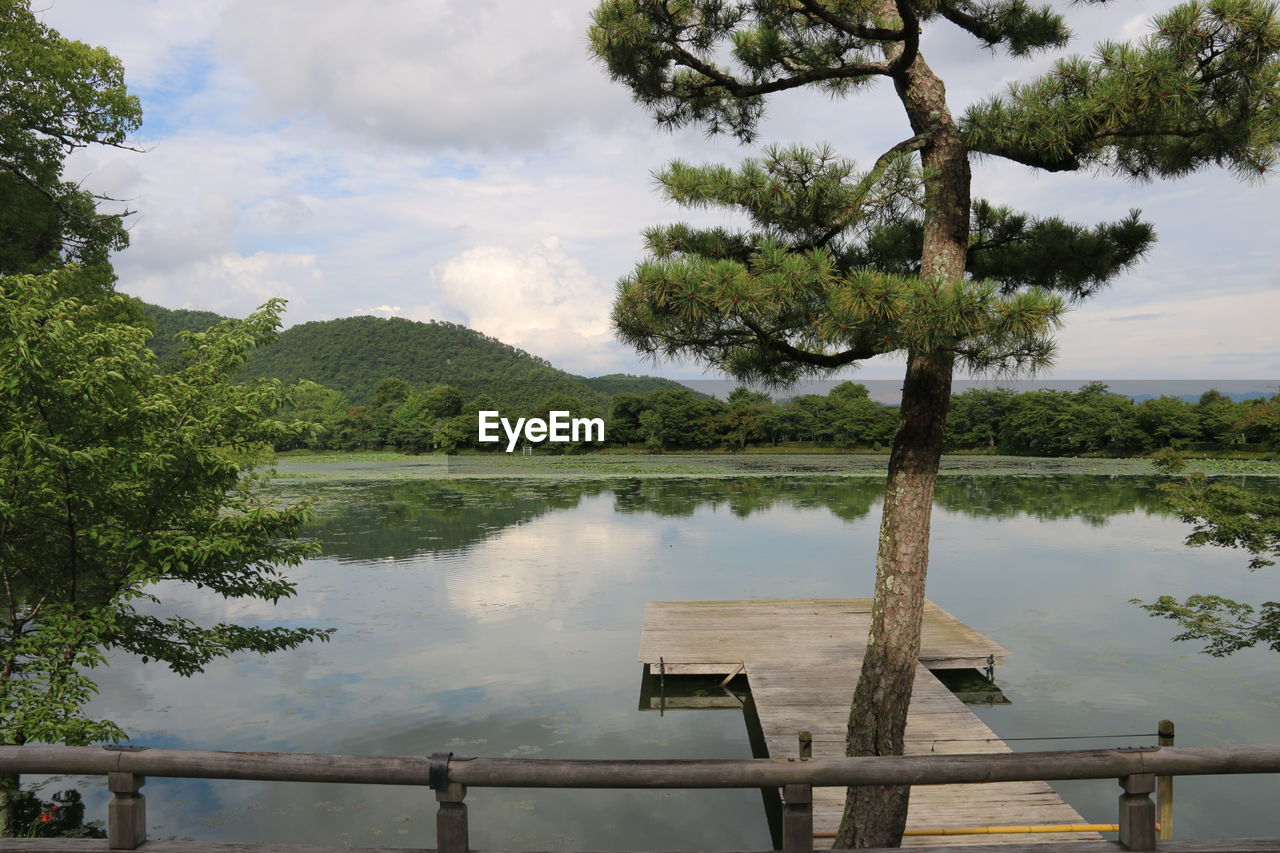 Lake with jetty and trees against cloudy sky