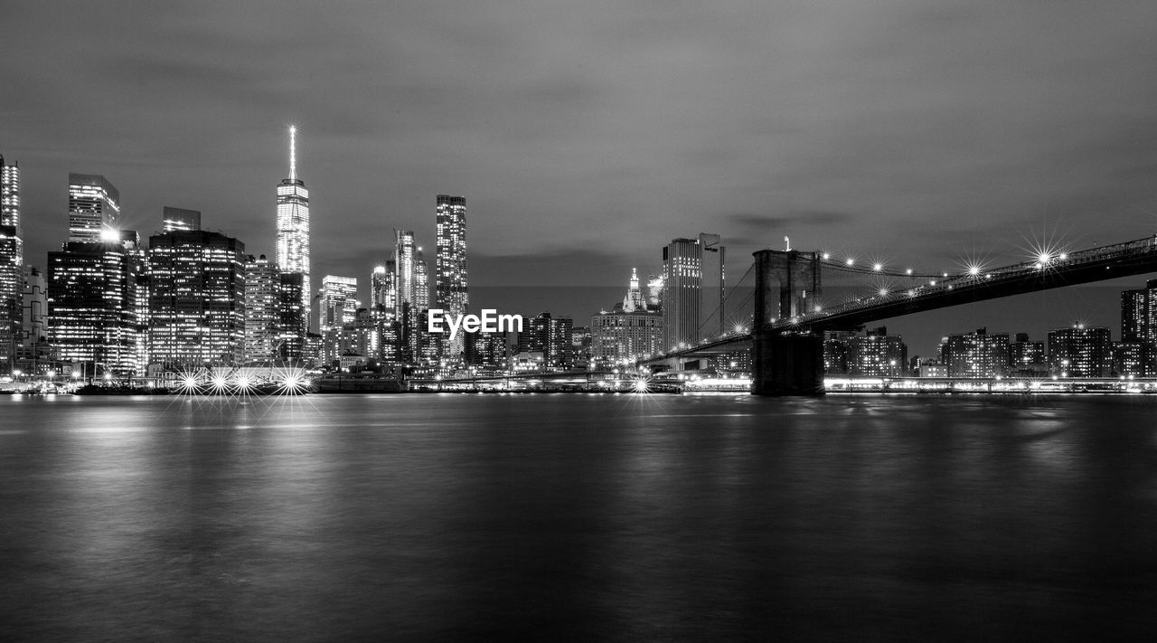 Brooklyn bridge over east river by illuminated city skyline against sky at dusk