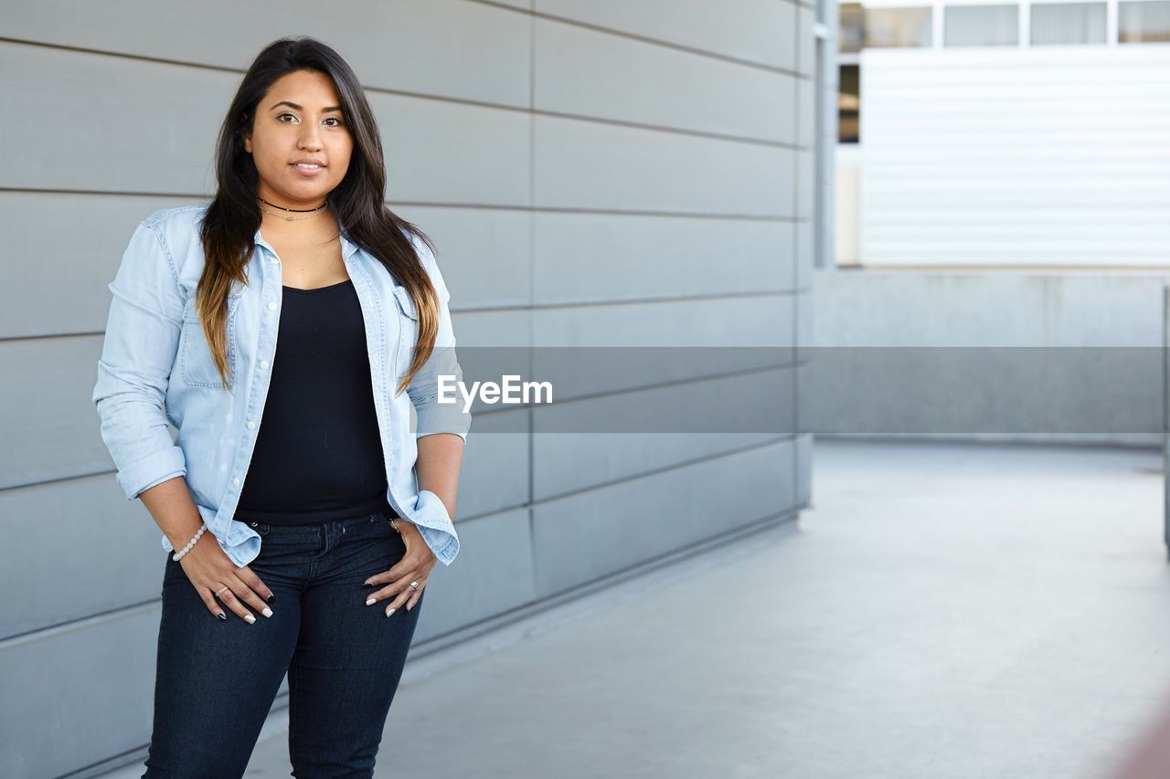 Portrait of young woman standing against wall