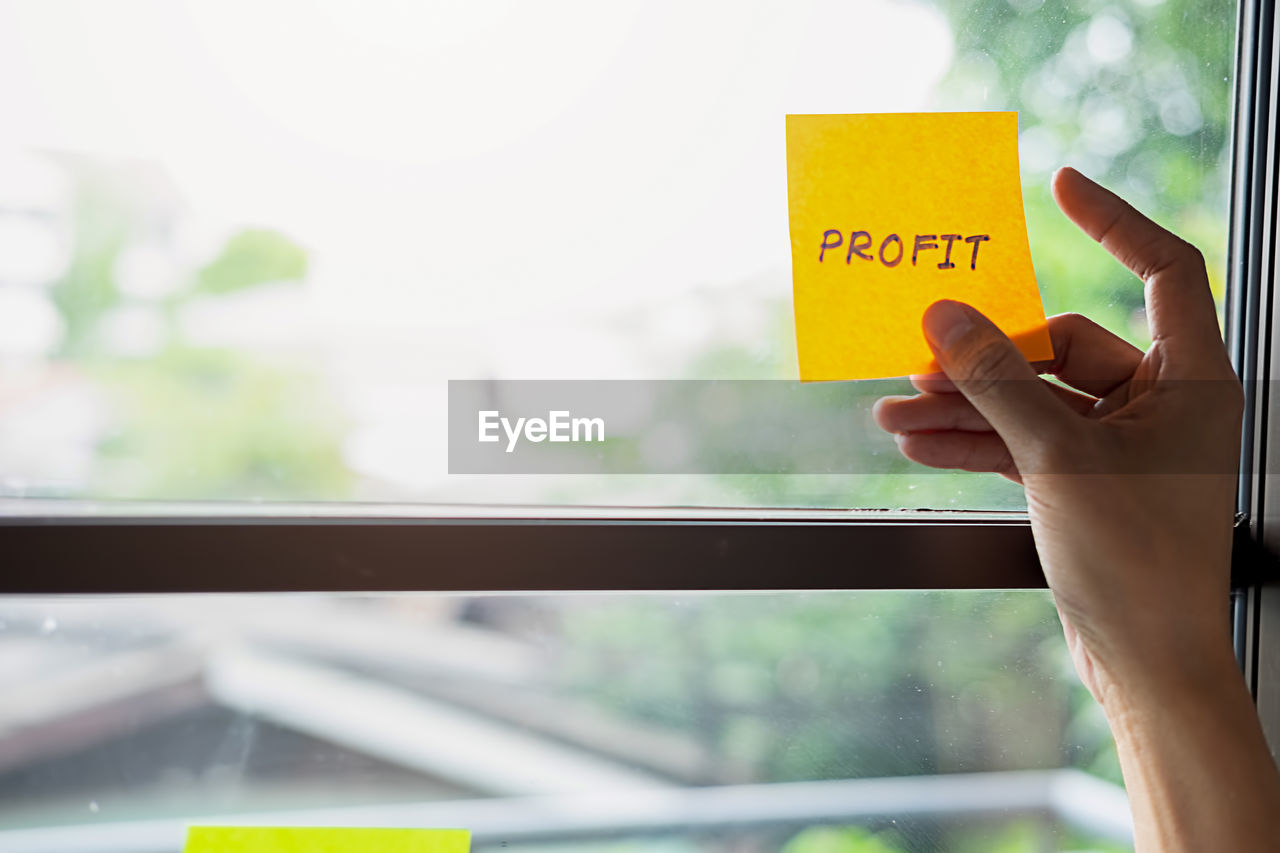 Cropped hand of businesswoman sticking profit text on window