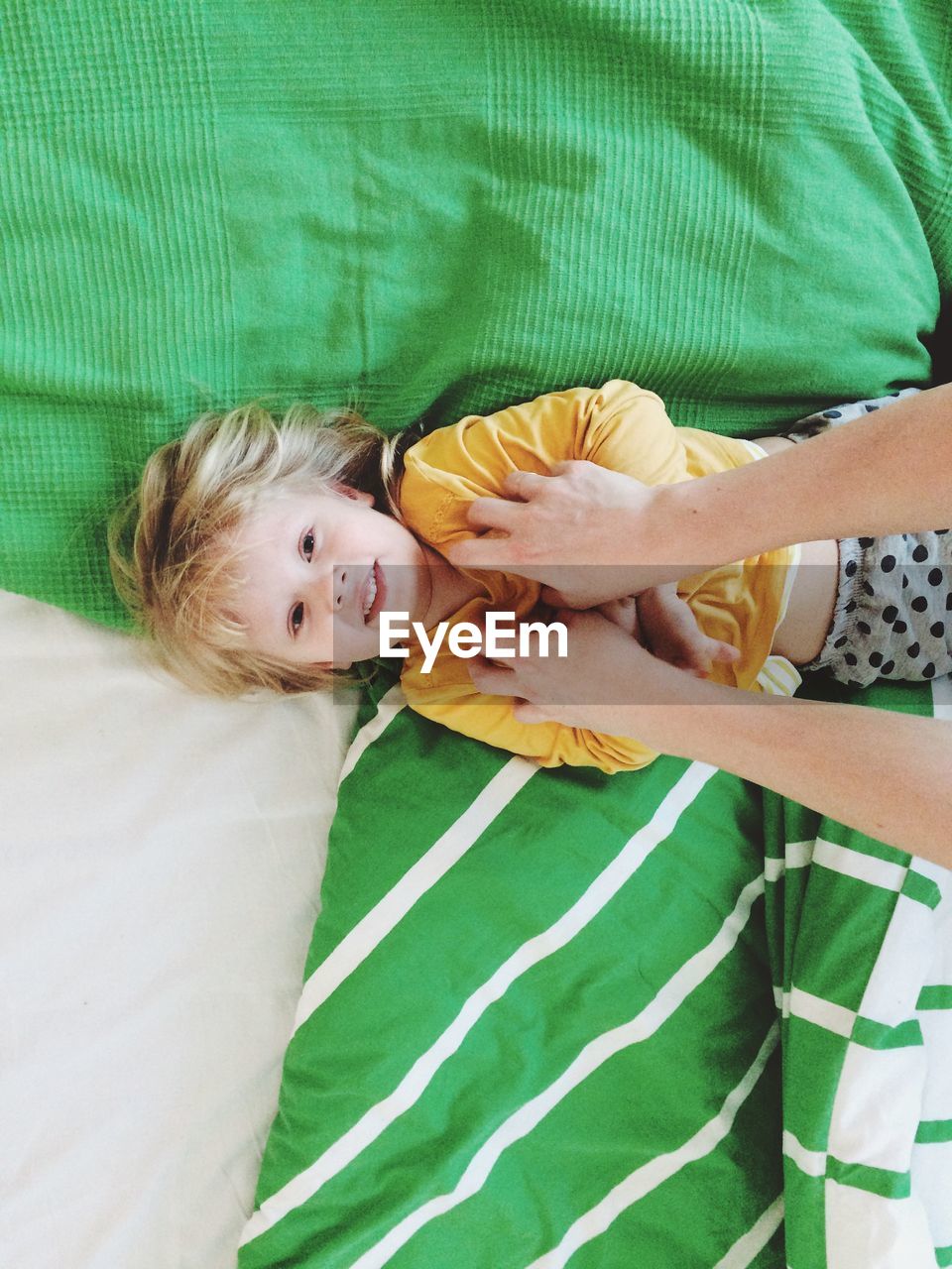 Cropped image of hands tickling girl on bed