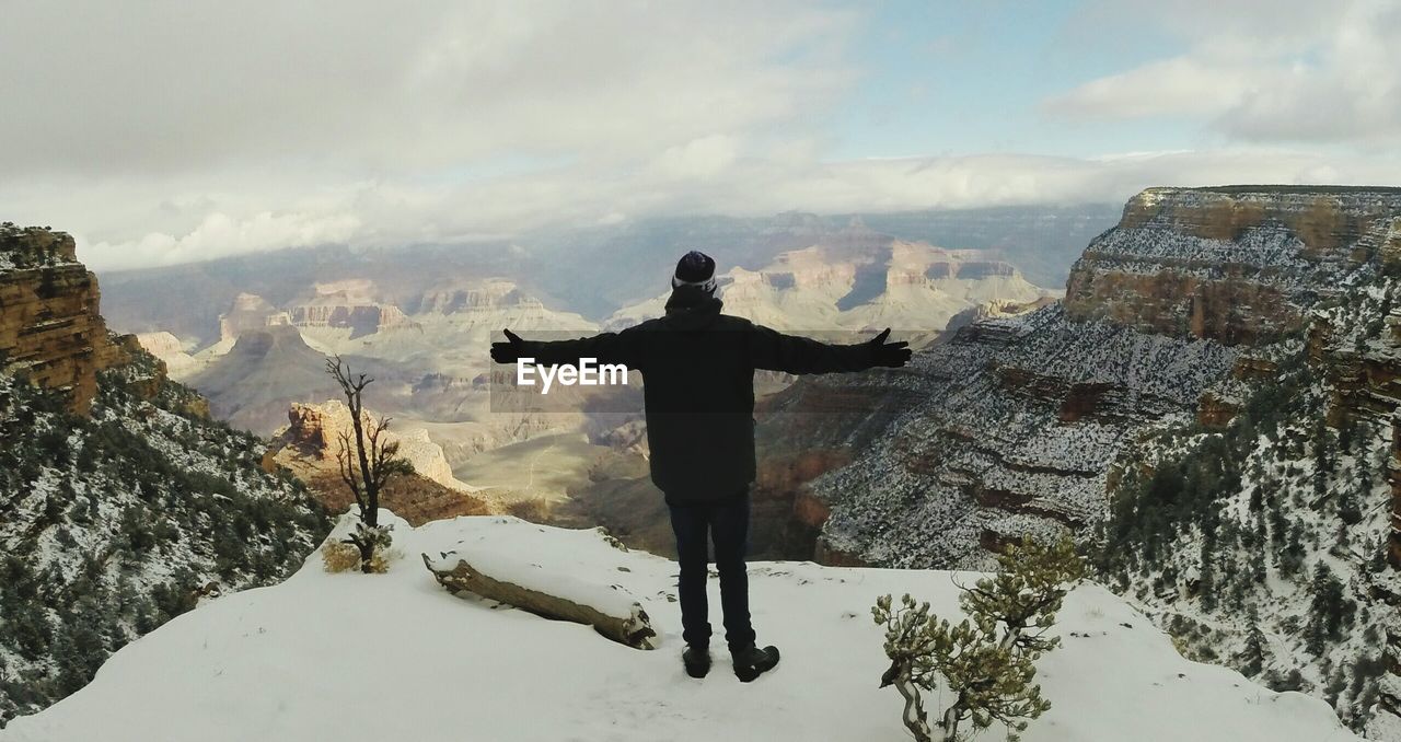 Rear view of person with arms outstretched at grand canyon against sky during winter