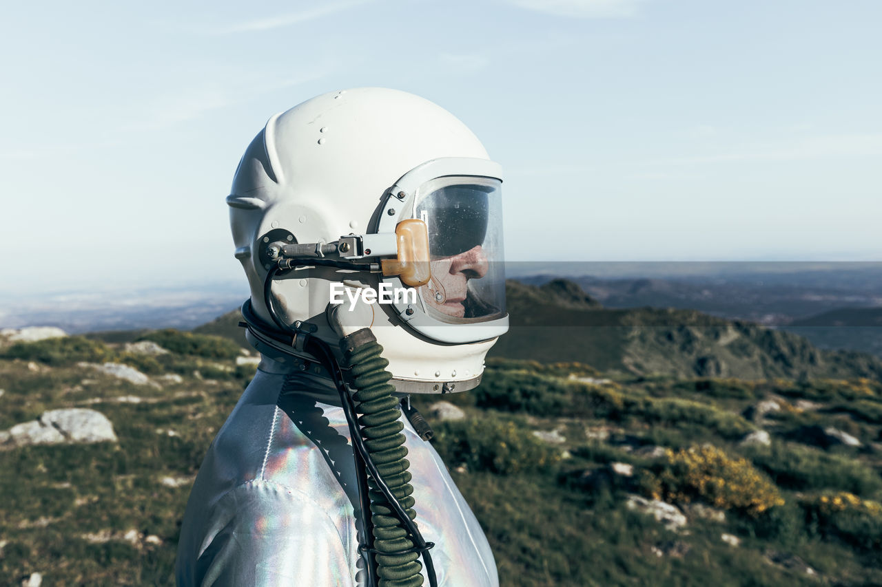 Side view male astronaut in spacesuit and helmet standing on grass and stones in highlands