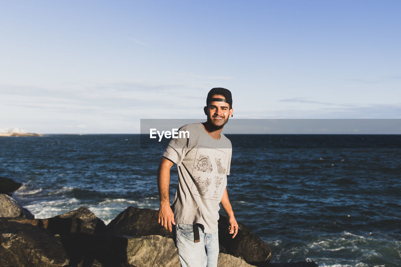 PORTRAIT OF YOUNG MAN STANDING ON BEACH