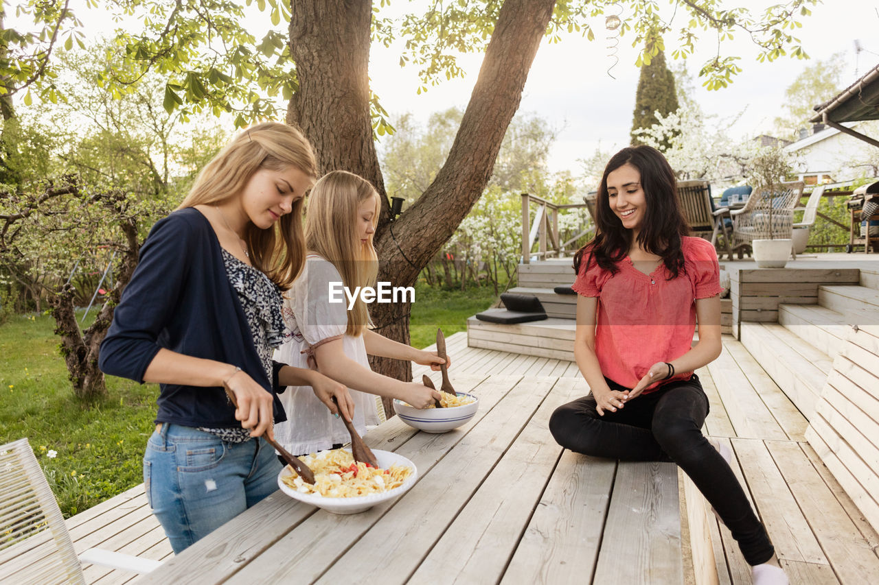 Teenage girls mixing salad at wooden table in yard