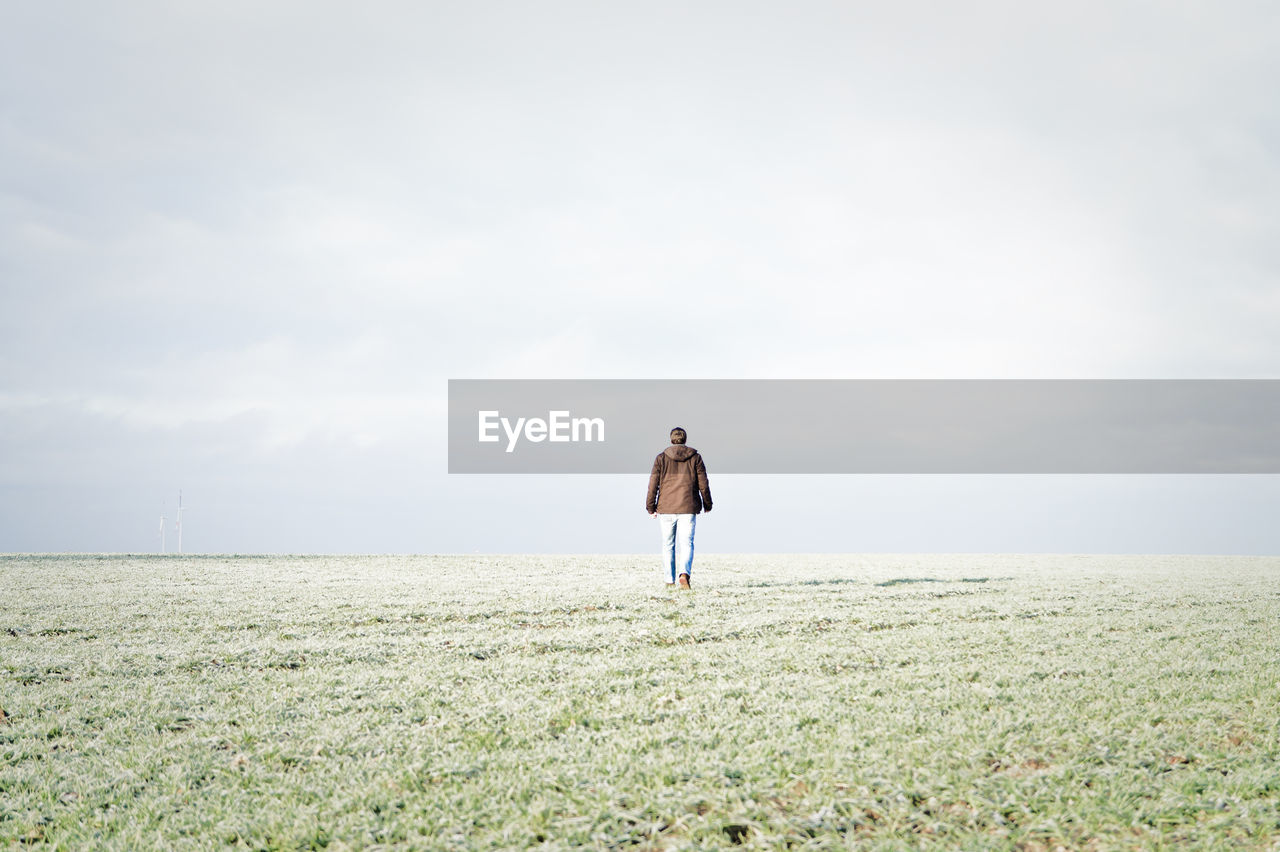 Rear view of man walking on grassy field against sky