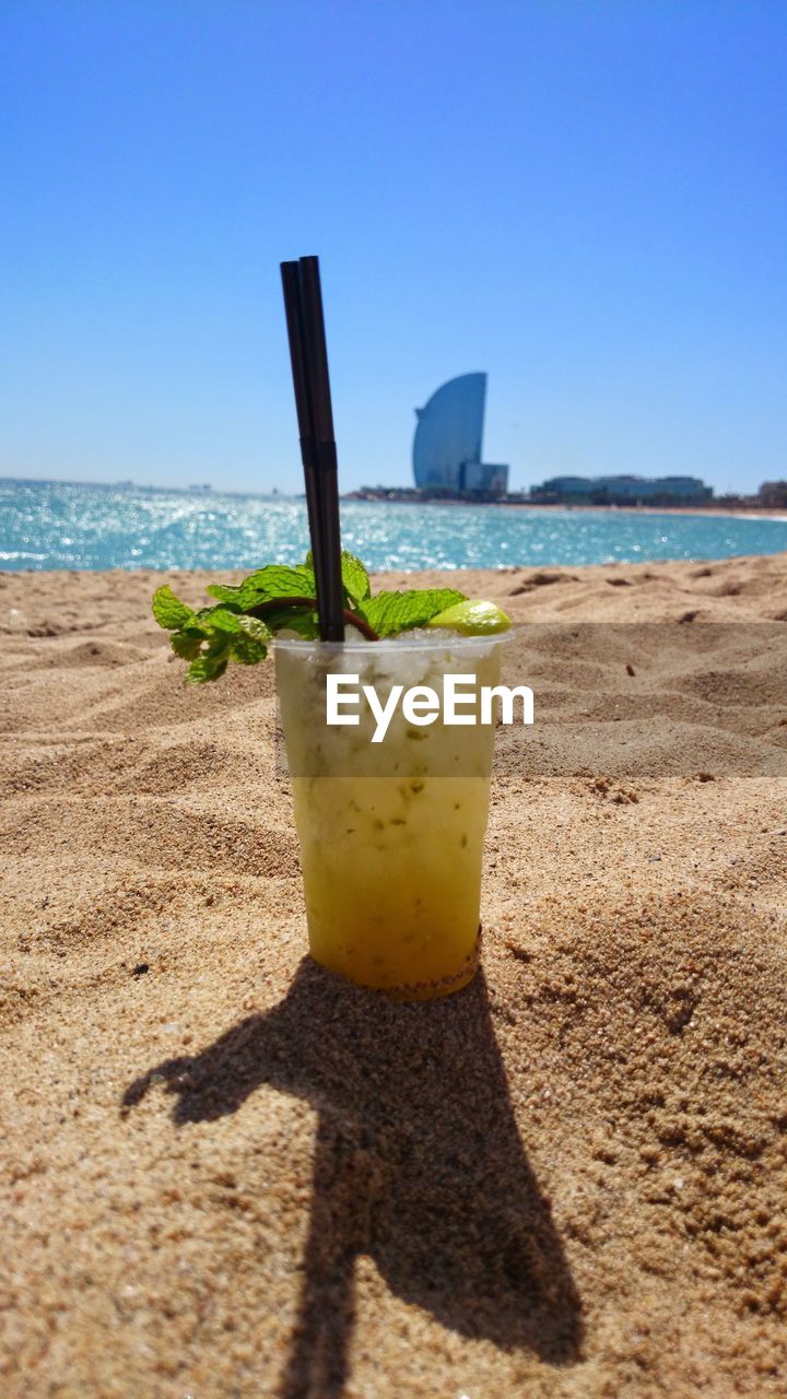 Disposable cup with drink at sandy beach against w barcelona