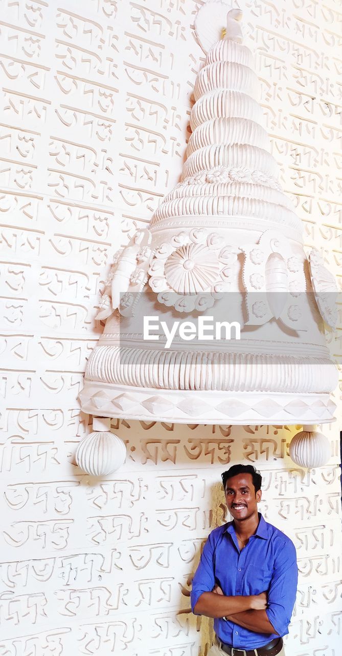 Portrait of a smiling young man standing against wall, look's like wearing a big bribe crown. 