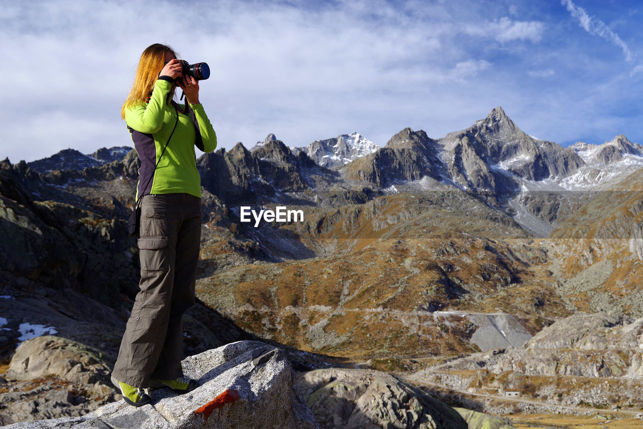 MAN PHOTOGRAPHING ON ROCK AGAINST MOUNTAINS