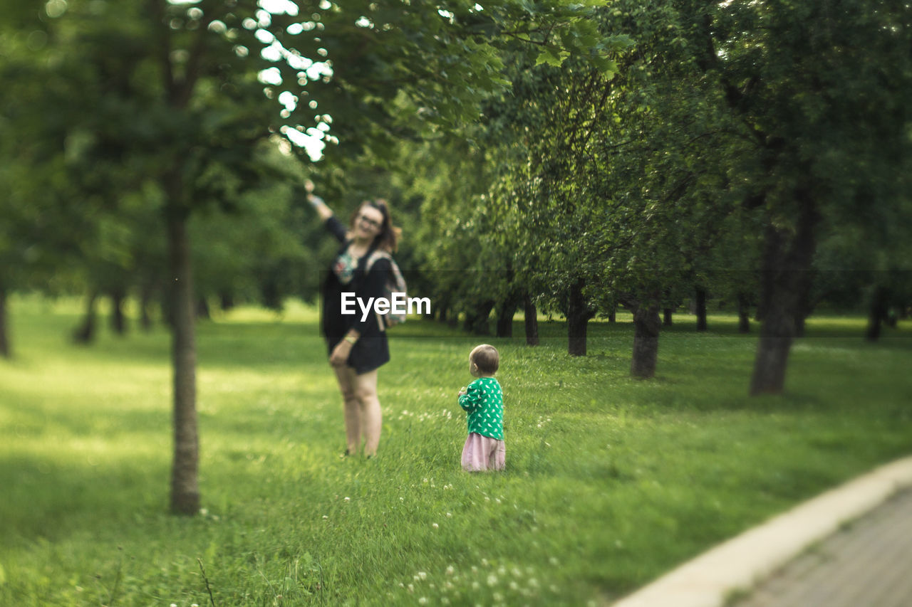 Baby girl looking at mother standing by tree at park