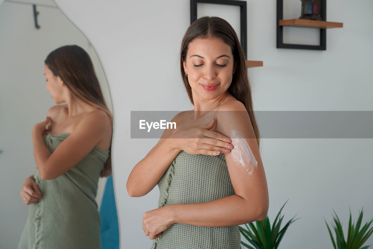 Relaxed pretty woman spreads body cream on arm and takes care of her skin at home