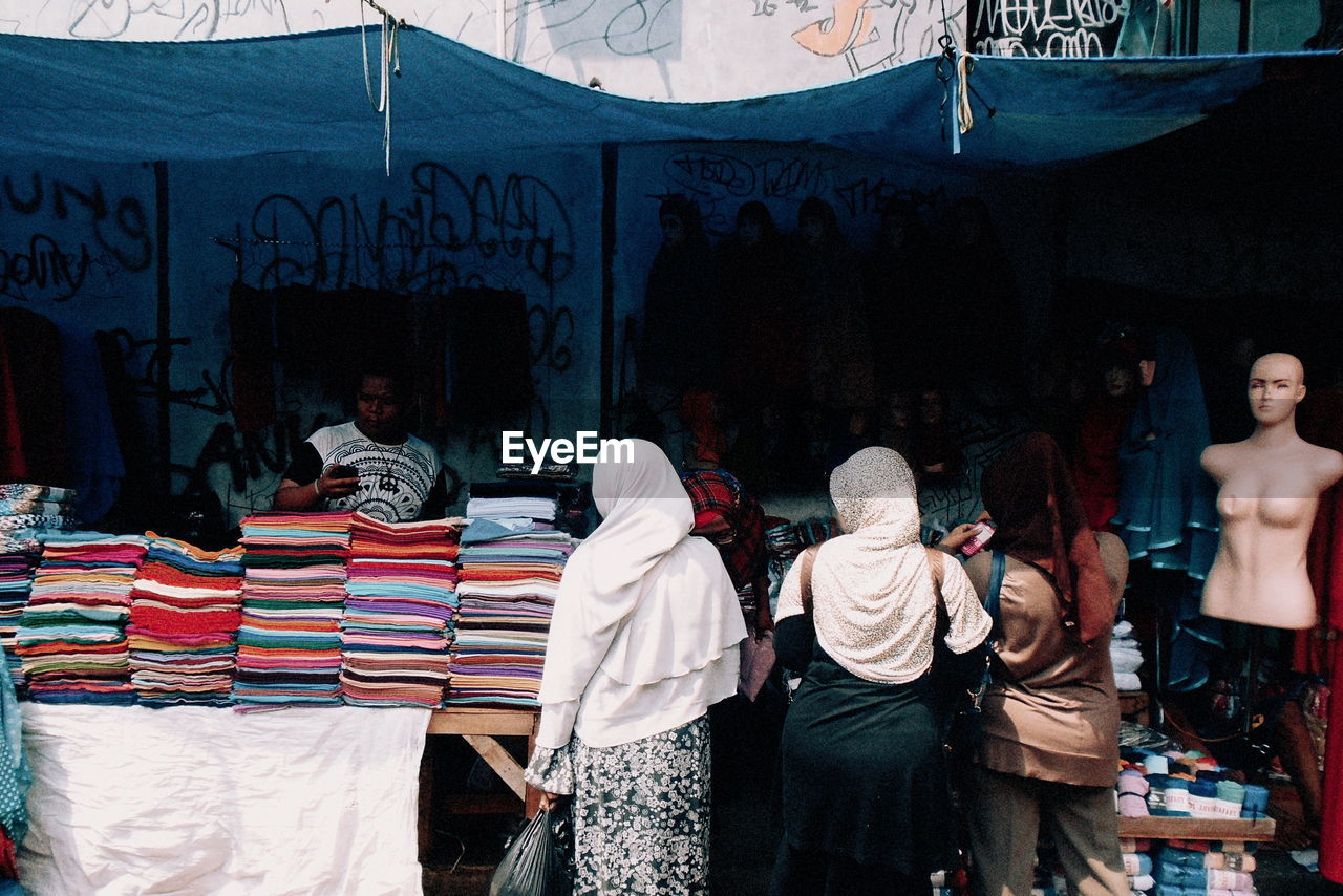 Rear view of woman in hijab standing by clothes at market stall