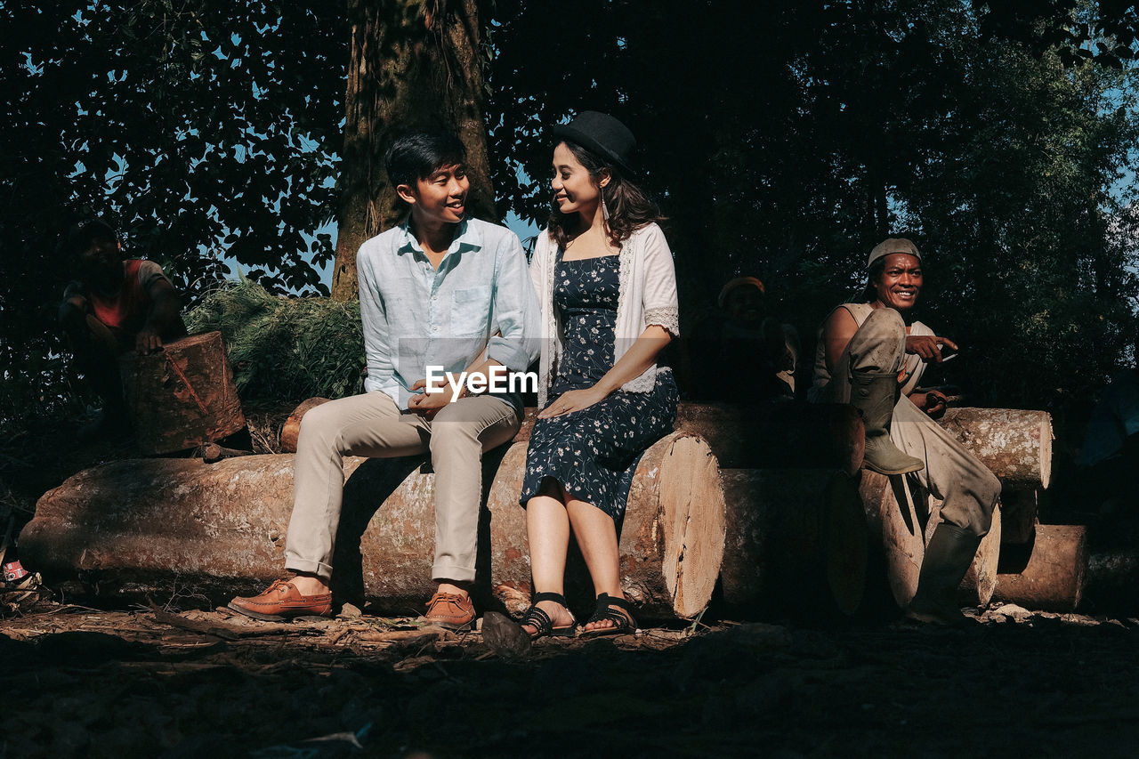 PEOPLE SITTING ON ROCK AGAINST TREES AND PLANTS