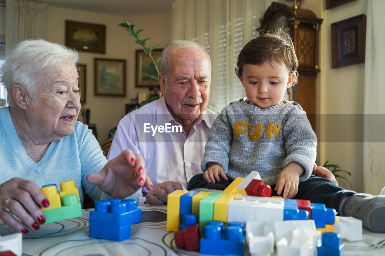 Great-grandparents and baby girl playing together with plastic building bricks at home