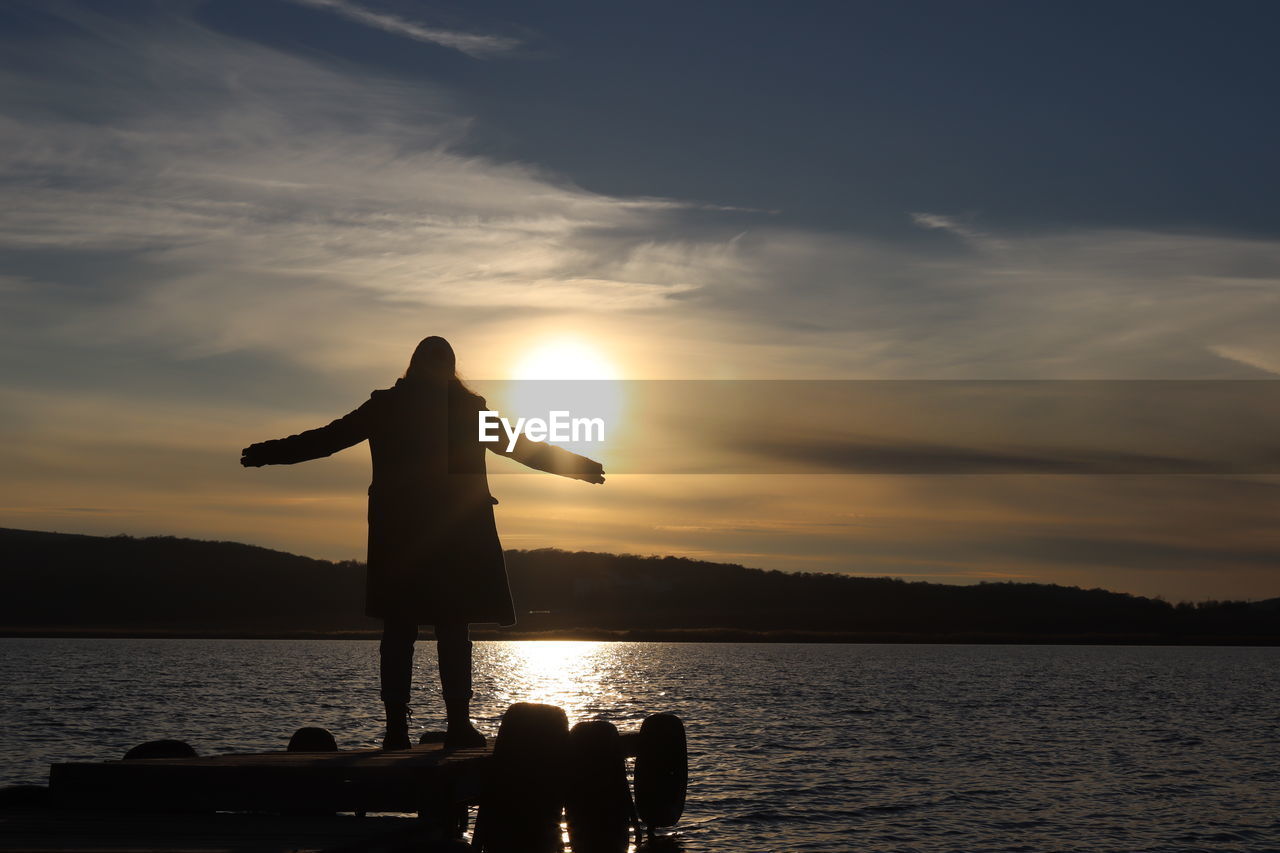 Silhouette man standing on shore against sky during sunset