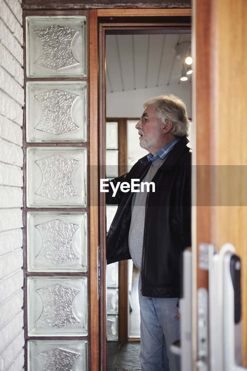 Side view of senior man standing in room seen through ajar