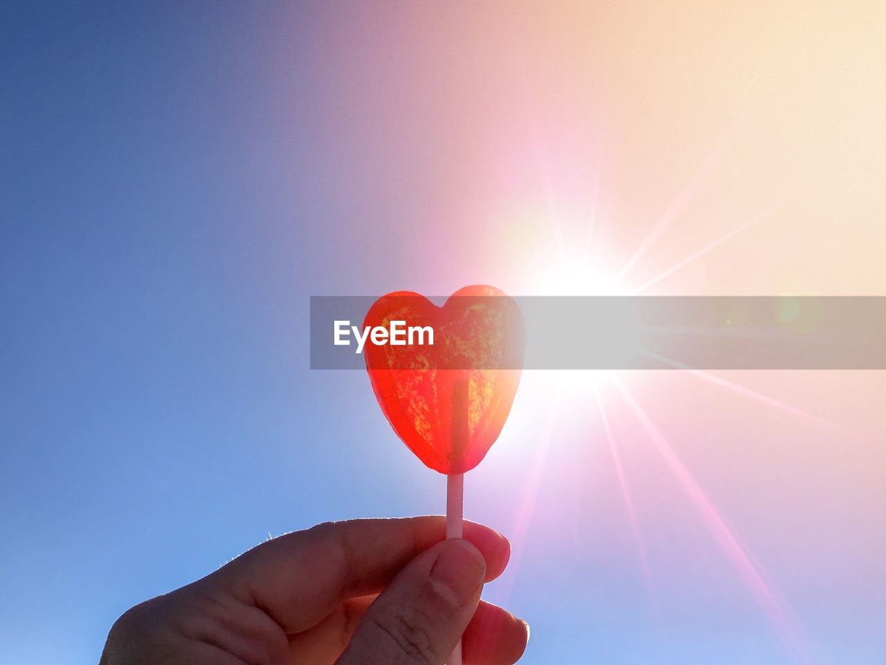 CLOSE-UP OF HAND HOLDING HEART SHAPE AGAINST SUN