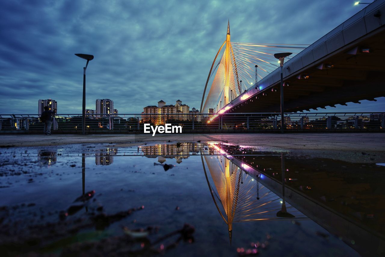 Illuminated bridge over river against sky in city