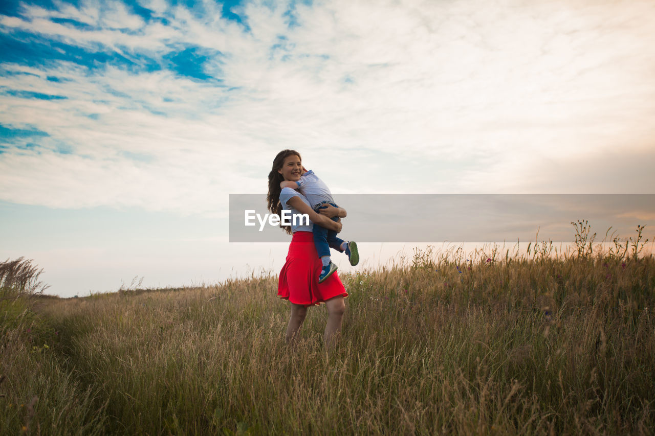 Girl carrying brother on field against sky