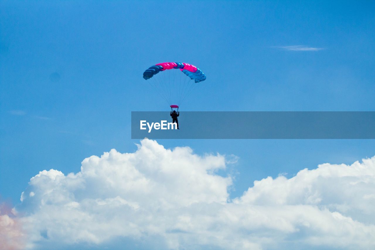 Low angle view of silhouette person paragliding against blue sky