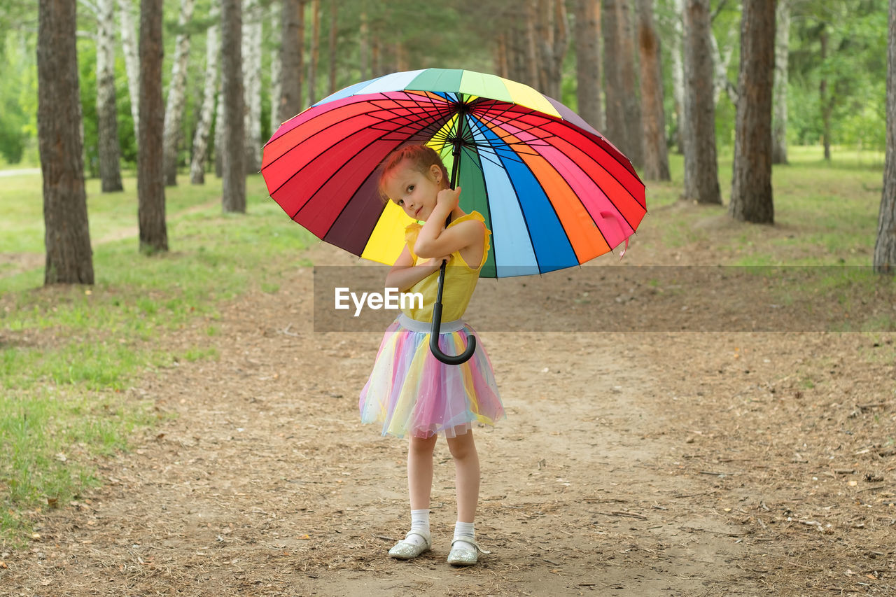 Happy funny girl holding rainbow umbrella. cute happy schoolgirl playing in rainy summer park. 