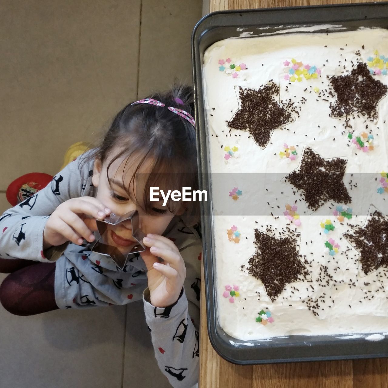 High angle view of playful girl with star shape pastry cutter by birthday cake on table