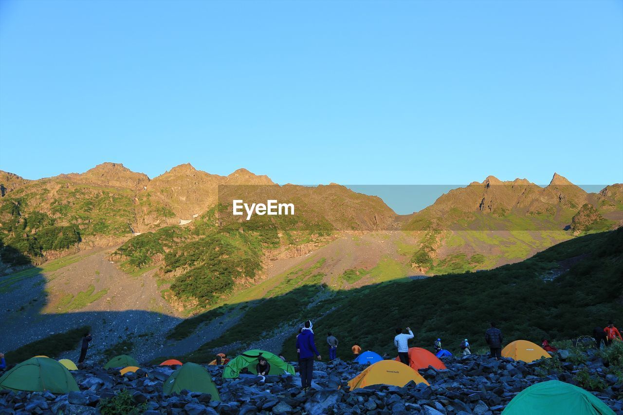 PEOPLE BY MOUNTAINS AGAINST CLEAR BLUE SKY