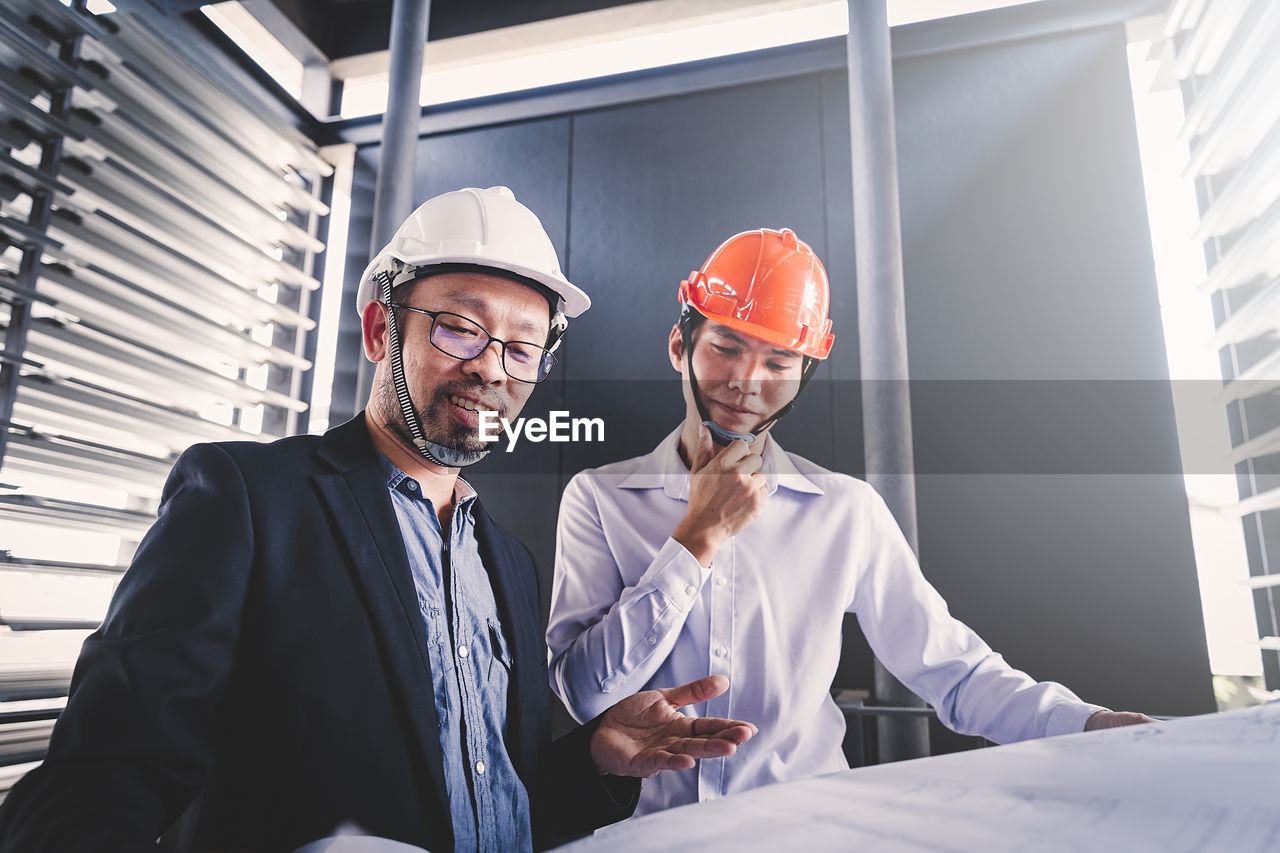 Low angle view of male architects discussing over blueprint at construction site