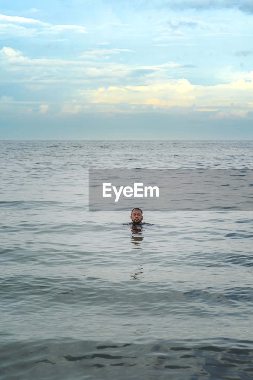 PERSON SWIMMING IN SEA AGAINST SKY