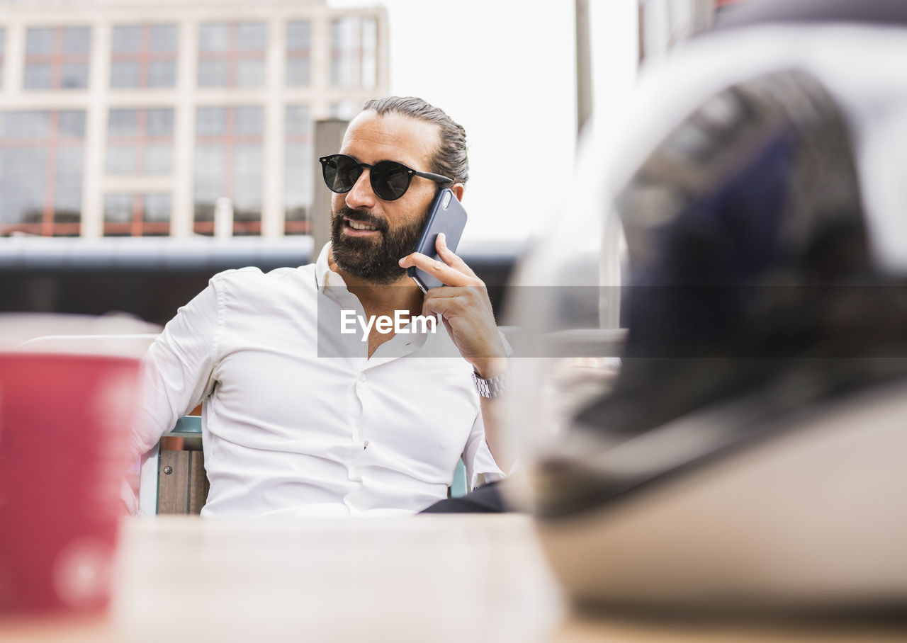 Portrait of bearded businessman wearing sunglasses talking outdoors on smart phone