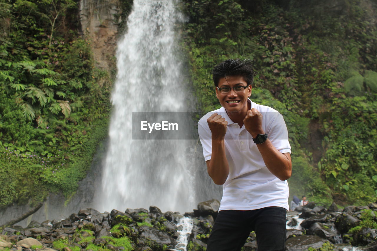 Portrait of smiling man standing against waterfall