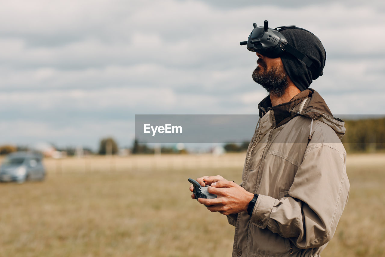 MAN HOLDING CAMERA WHILE STANDING ON FIELD