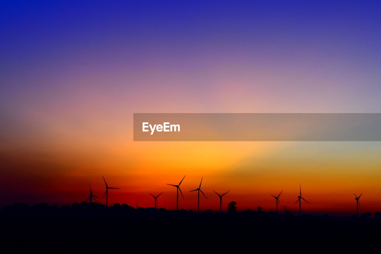 SILHOUETTE OF WIND TURBINES ON LAND AGAINST SKY DURING SUNSET