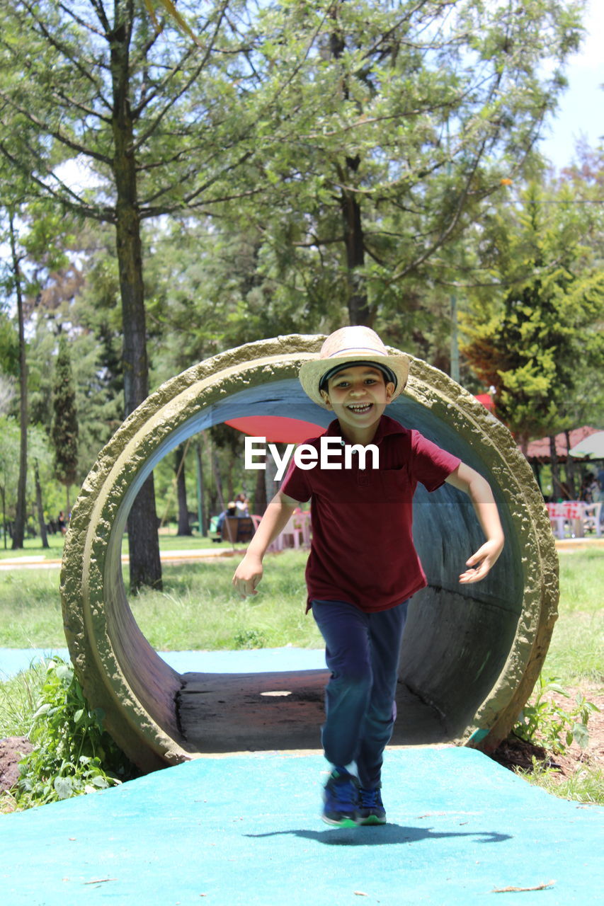 Full length portrait of smiling boy walking by tunnel in park