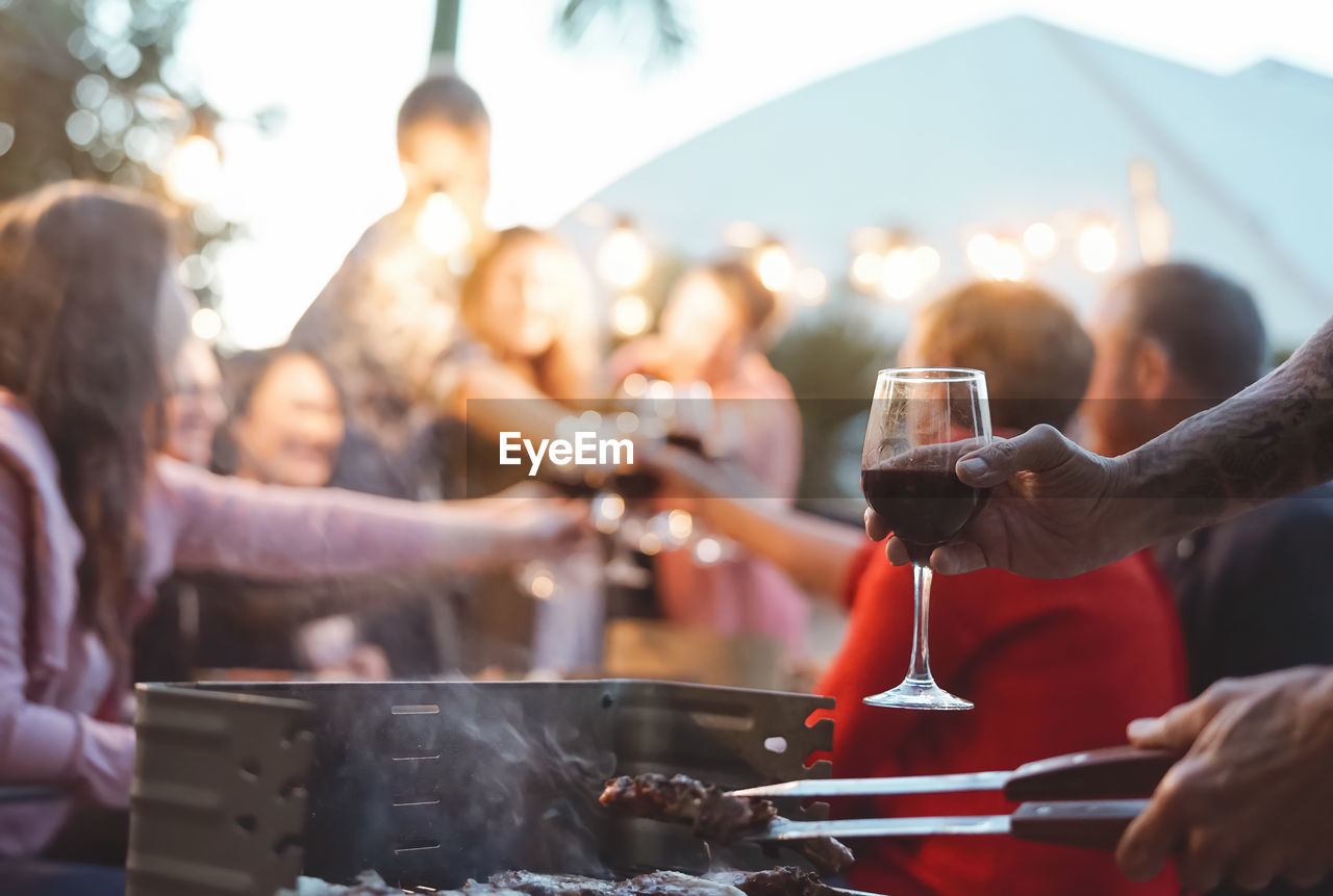 Cropped hand holding drinking glass while cooking food over grill