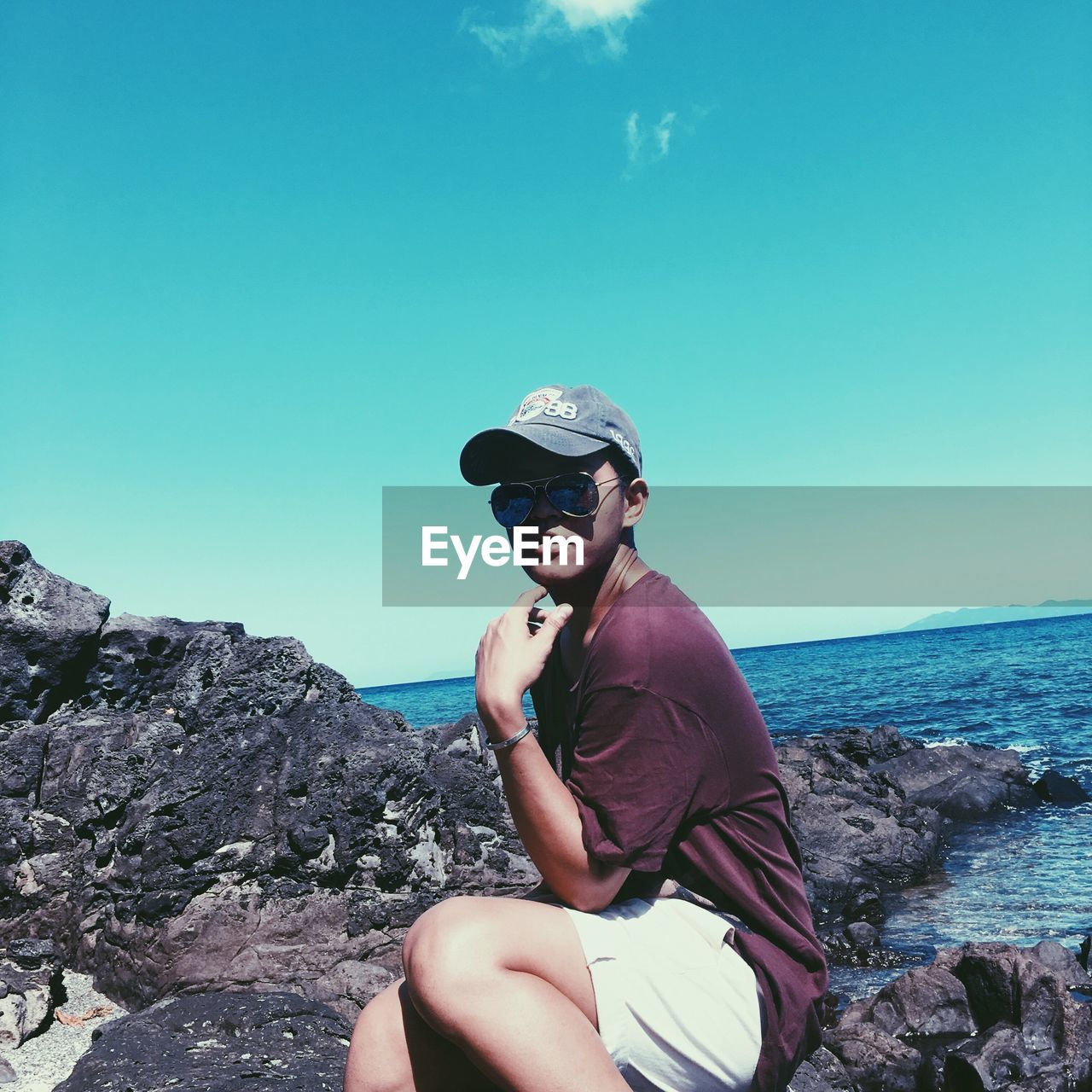 WOMAN SITTING ON ROCK BY SEA AGAINST CLEAR SKY