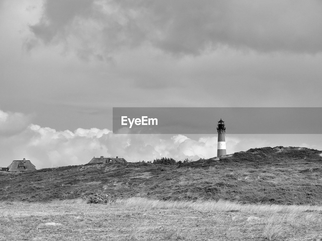 Lighthouse on field by building against sky