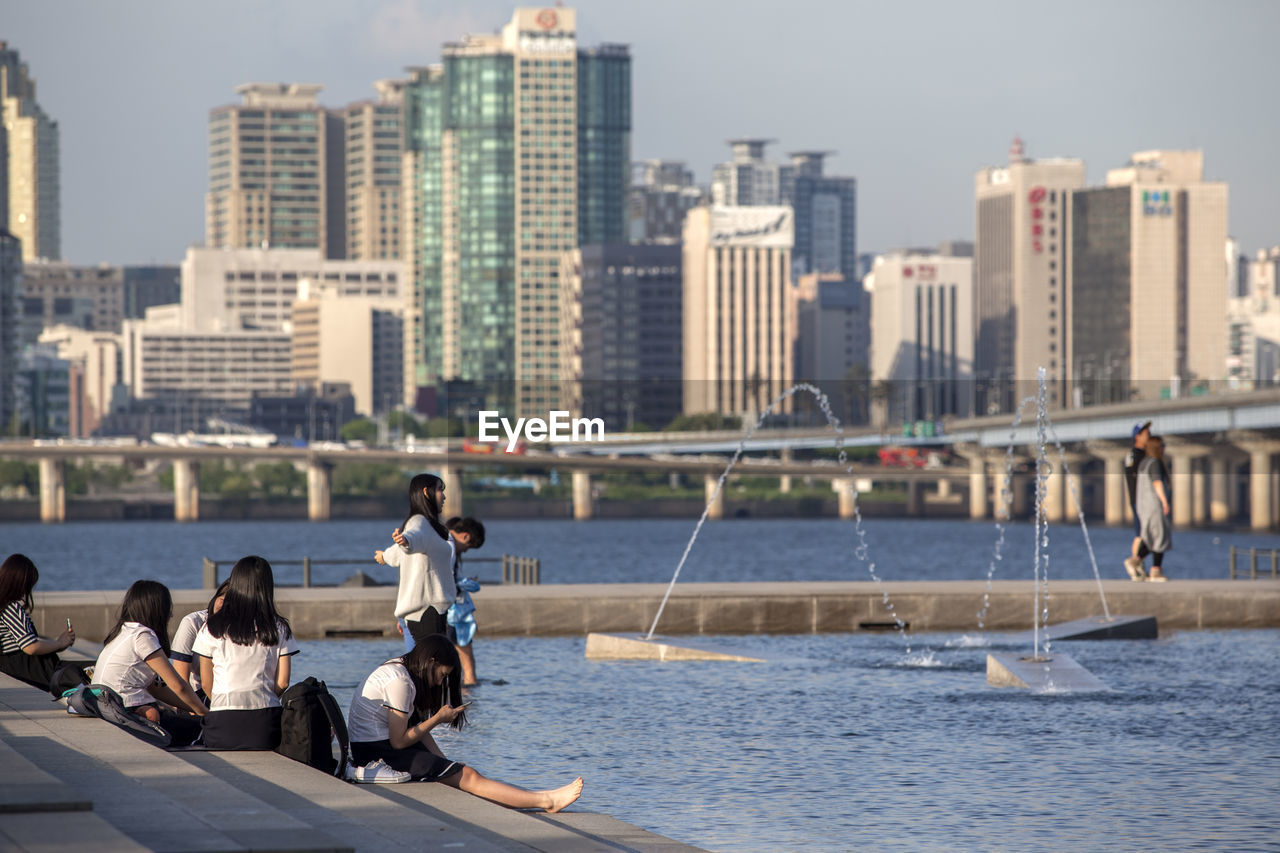 People on steps by han river against buildings in city