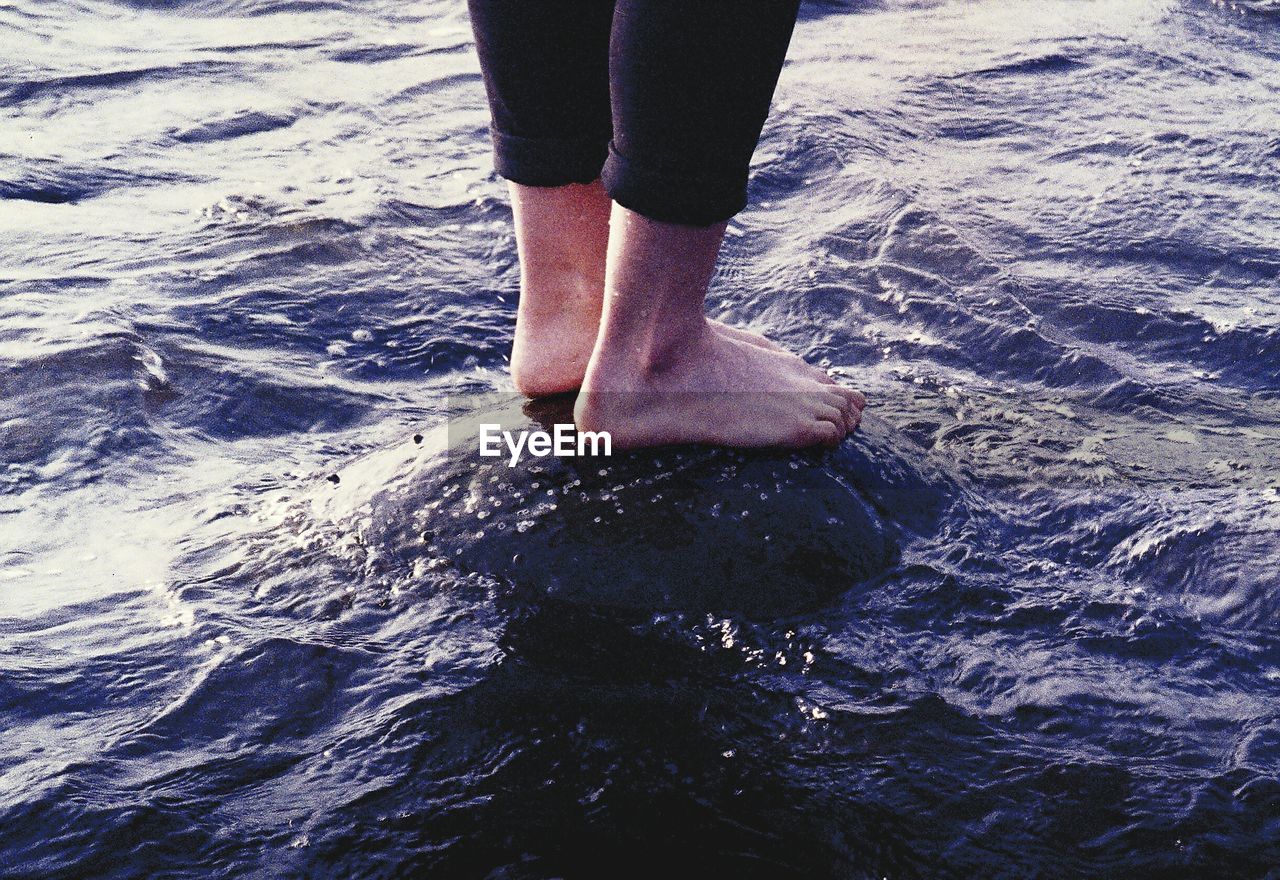 Legs of woman standing on rock in water