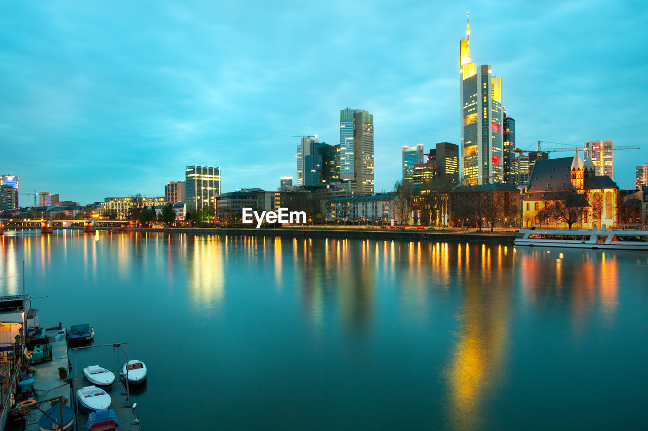 Illuminated buildings by river against sky in city