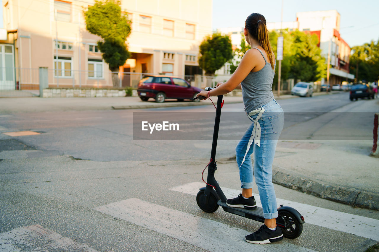 Young woman standing on electric push scooter on street