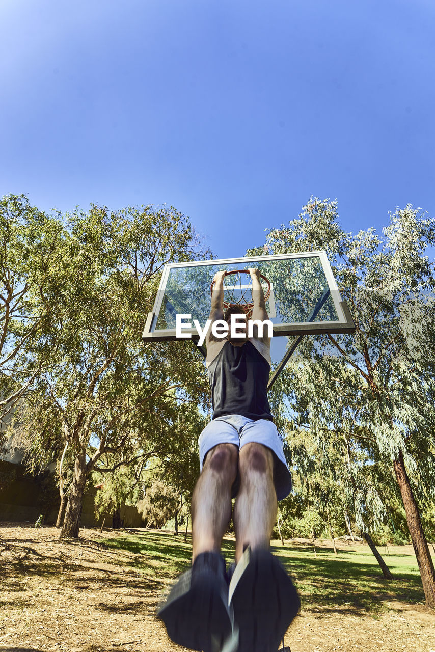 Low angle view of man hanging from basketball hoop