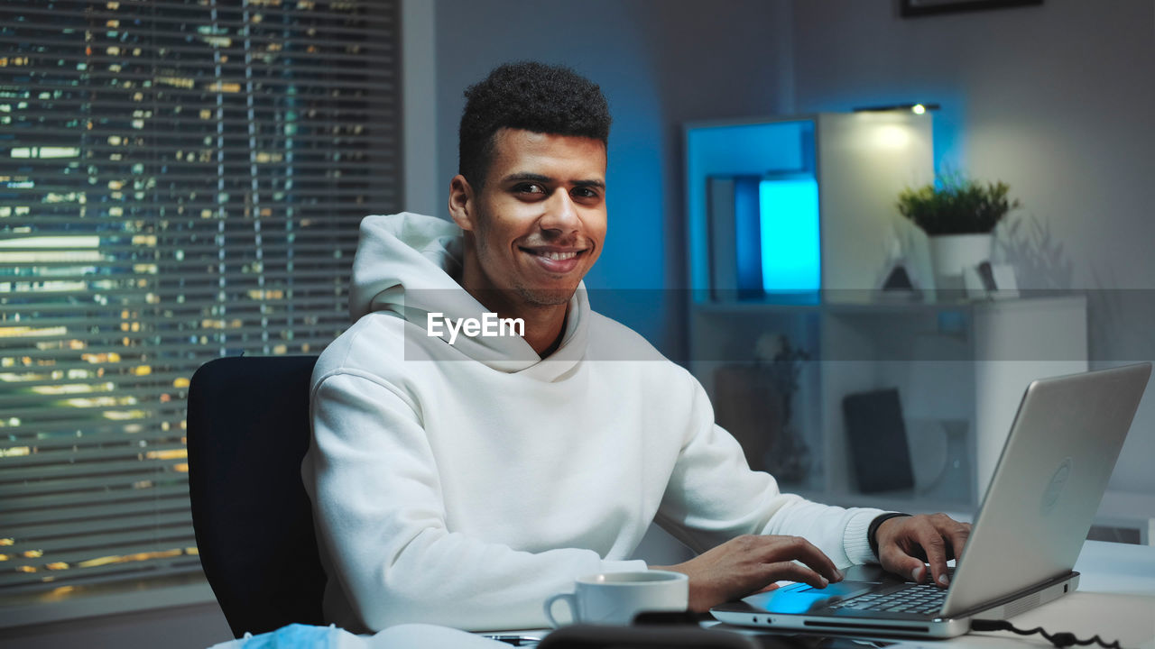 portrait of young man using laptop while sitting on table in office