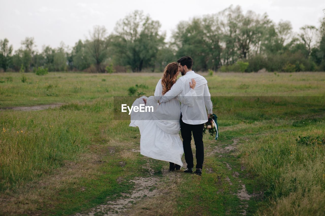 Newlywed couple walking on field against sky