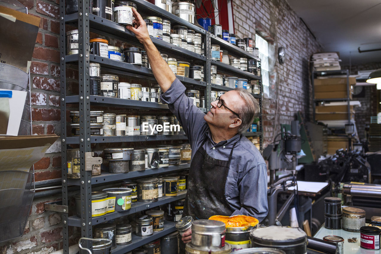 Man picking up ink container from shelves at letterpress workshop