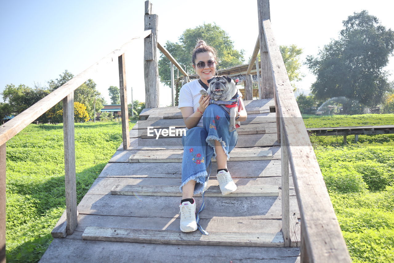 Mature woman with dog sitting on wooden built structure