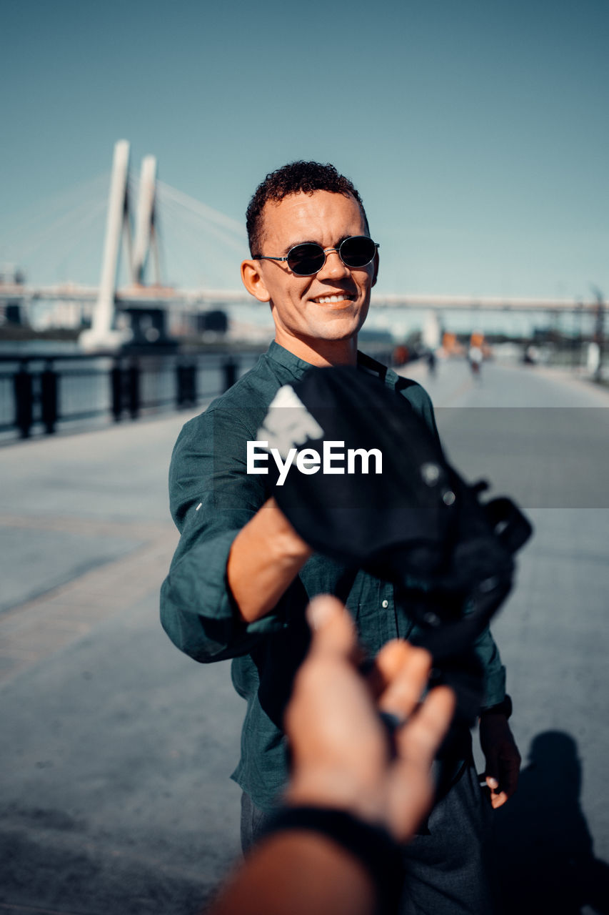 PORTRAIT OF MAN HOLDING SUNGLASSES WHILE STANDING BY CAR